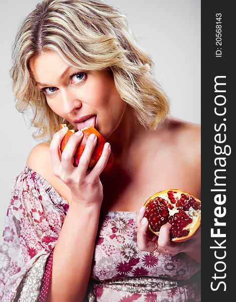 Blonde woman licking pomegranate on grey