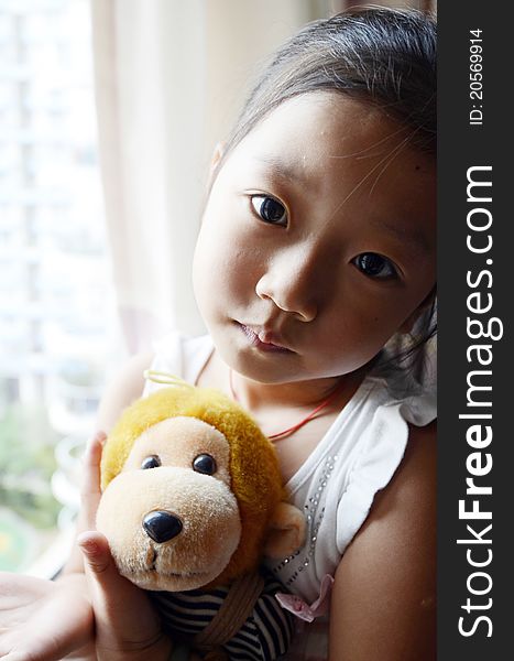 Bright picture of adorable chinese girl Holding the Toy Monkey near the windows. Bright picture of adorable chinese girl Holding the Toy Monkey near the windows