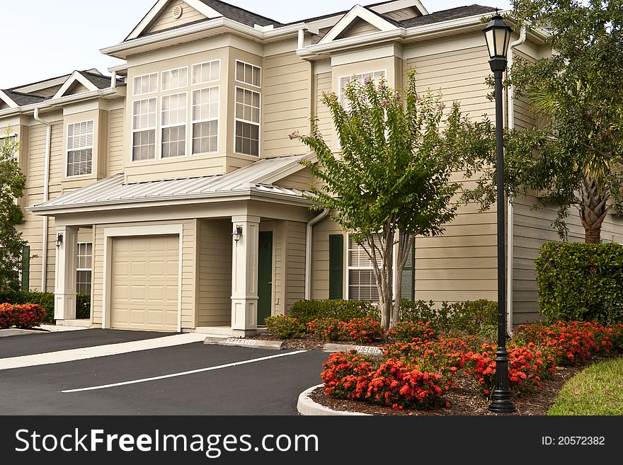 Two-story condos in a row with red flowers, garages and parking spaces, surrounded by tropical landscaping