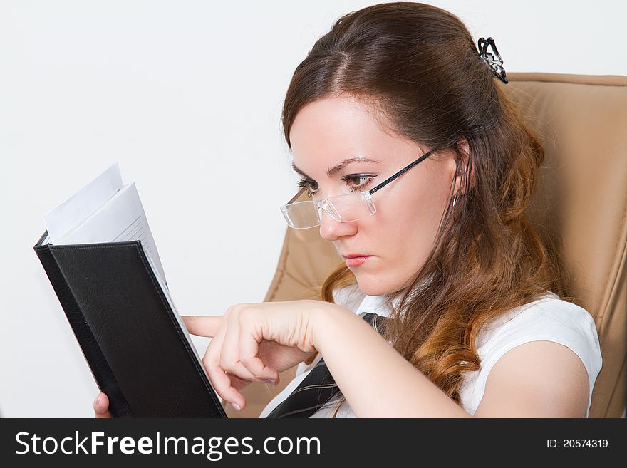 Business woman with long hair wearing glasses points a finger in a notebook in the office. Business woman with long hair wearing glasses points a finger in a notebook in the office