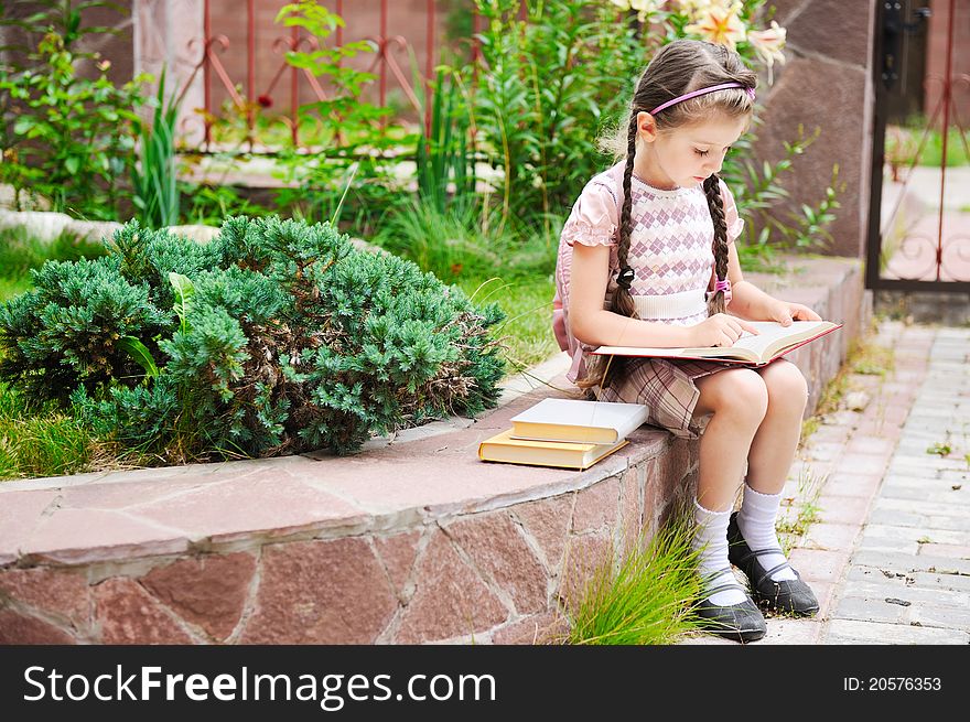 Young school girl with pink bagpack sits reading the book. Young school girl with pink bagpack sits reading the book