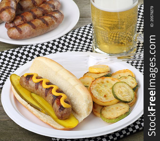 Grilled bratwurst with mustard and pickles on a bun and fried squash. Grilled bratwurst with mustard and pickles on a bun and fried squash