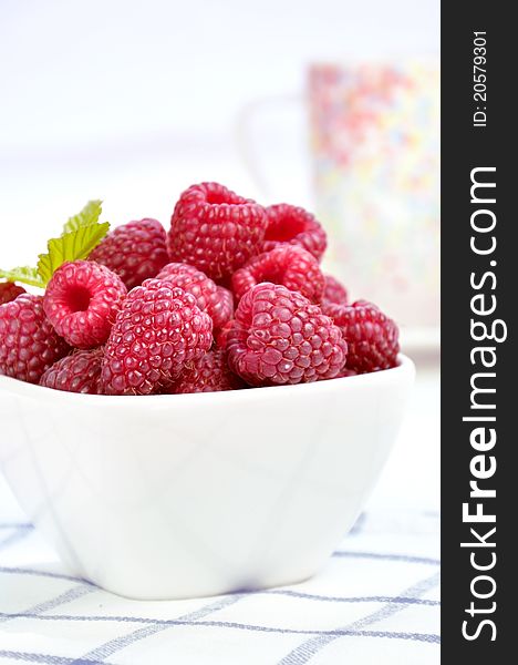 Raspberries in a white bowl on a napkin in a lattice