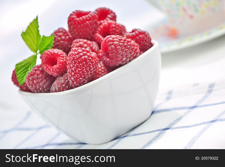 Raspberries in a white bowl on a napkin in a lattice