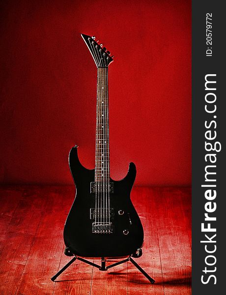 A black electric guitar on a red grainy background. A grainy scenery alltogether with powerful contrasts and shadows. A black electric guitar on a red grainy background. A grainy scenery alltogether with powerful contrasts and shadows.