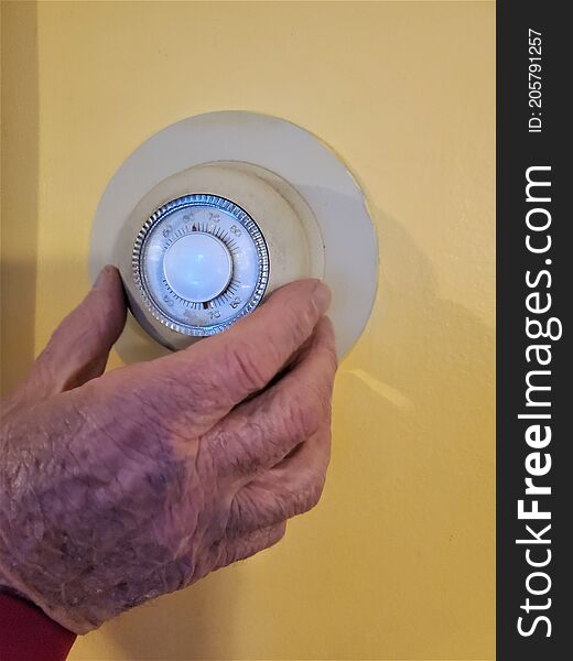 Home heating unit with temperatures in degrees Fahrenheit and dial knob is held by male senior hand.  Wrinkles and dark spots show on large fingers and back of body part.  Cold temperature set at low 62 degrees. Home heating unit with temperatures in degrees Fahrenheit and dial knob is held by male senior hand.  Wrinkles and dark spots show on large fingers and back of body part.  Cold temperature set at low 62 degrees