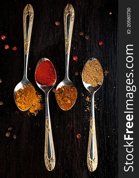 Four silver teaspoons with mix of the spices on black table