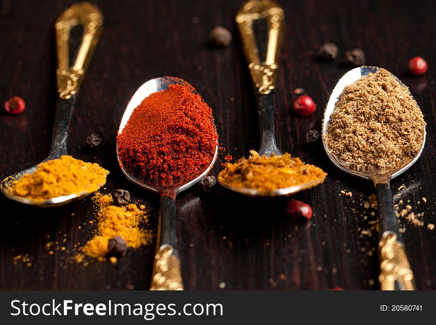 Four silver teaspoons with set of the spices on black table. Four silver teaspoons with set of the spices on black table