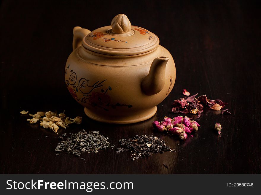 Ceramic teapot with dry tea variation on black table. Ceramic teapot with dry tea variation on black table