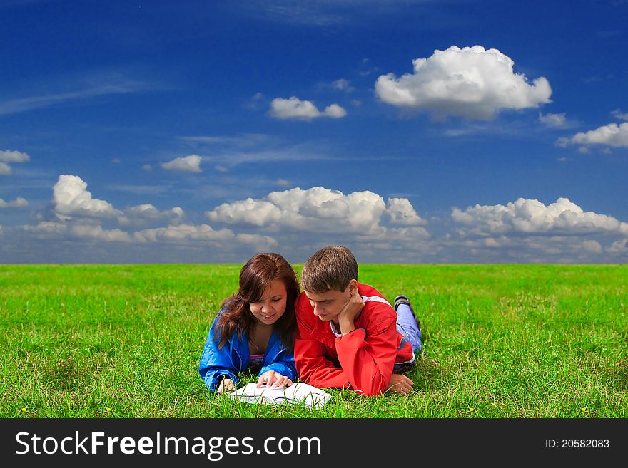 Young man and woman reading book together outdoors on grass. Young man and woman reading book together outdoors on grass