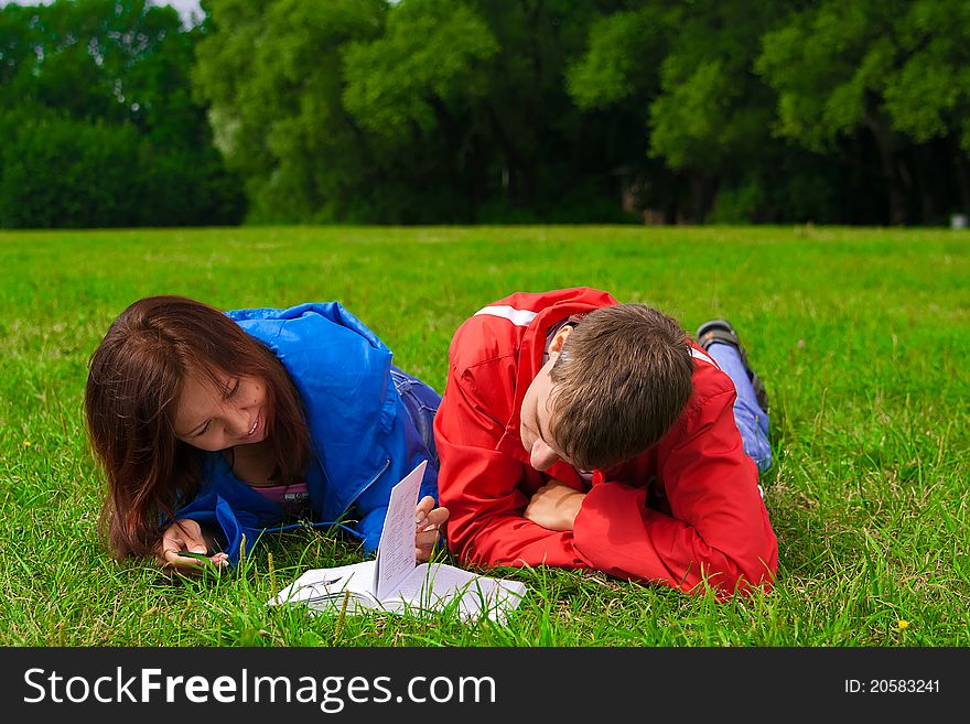 Young man and woman reading book together outdoors on grass. Young man and woman reading book together outdoors on grass