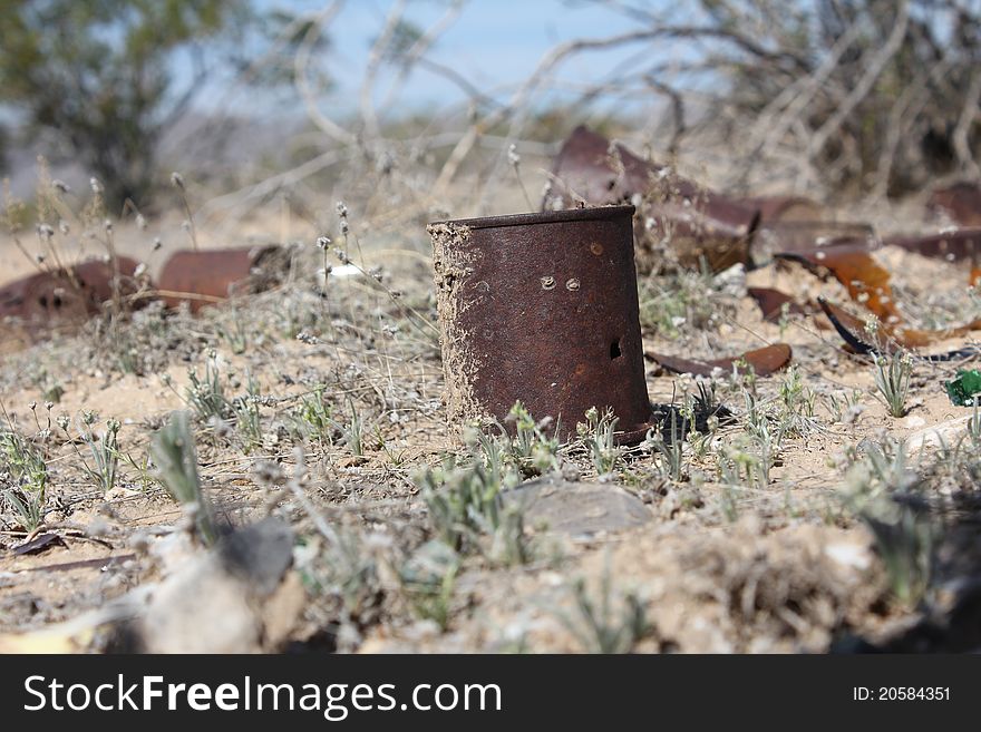 Rusty cans sit in an empty desert field.  A few scattered broken bottles litter the ground as well.