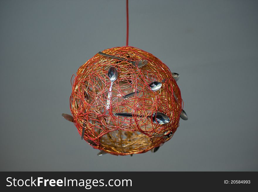 Red round lamp with spoons against a grey background