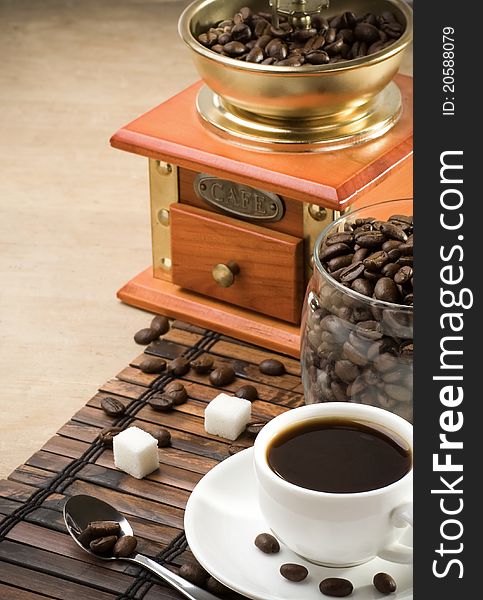 Cup of coffee, grinder and jar full of beans on wood