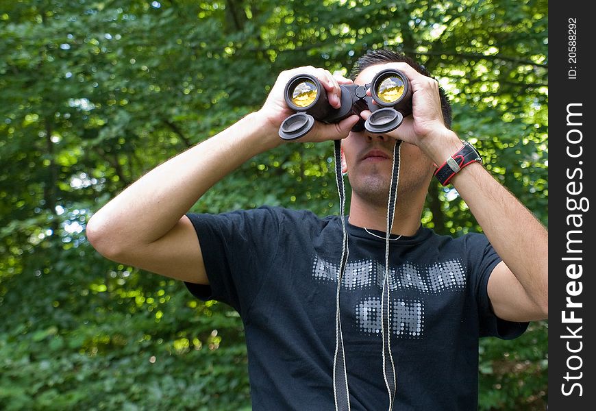 Young man looking through binoculars while hiking out in nature
