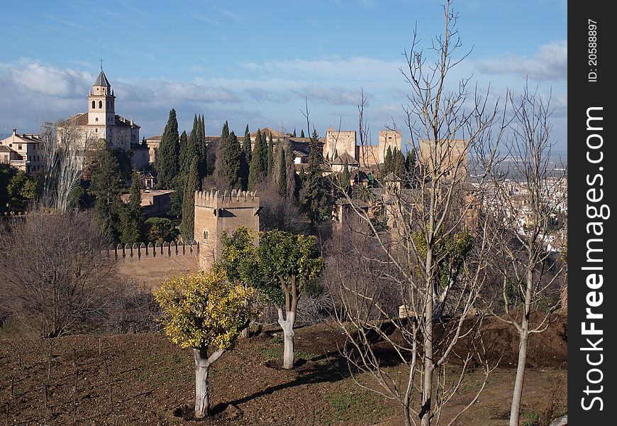 The fortifications of the Alhambra and its surrounding gardens lit up by the early morning sun against a blue sky. The fortifications of the Alhambra and its surrounding gardens lit up by the early morning sun against a blue sky.