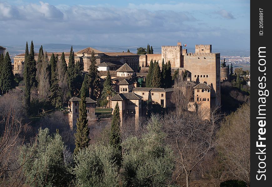 The fortifications of the Alhambra and its surrounding gardens lit up by the early morning sun against a blue sky. The fortifications of the Alhambra and its surrounding gardens lit up by the early morning sun against a blue sky.