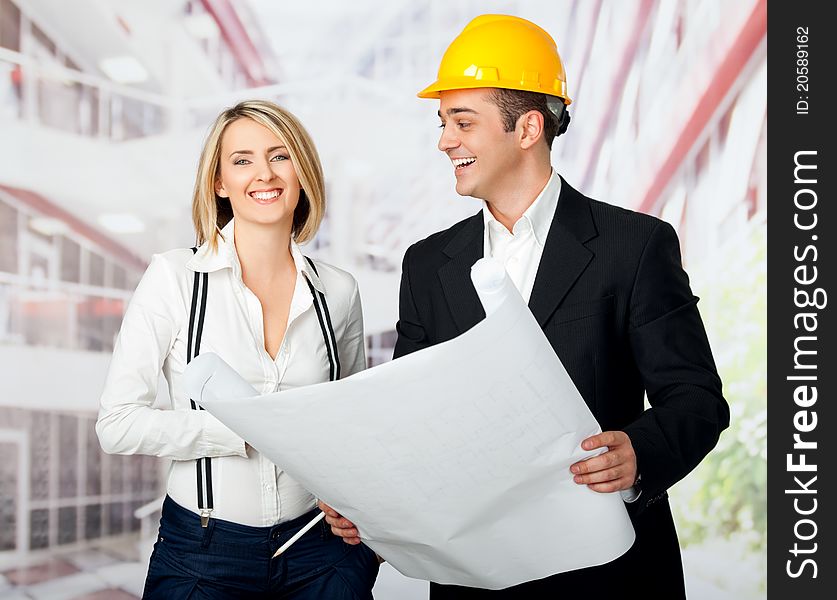 Male and female architects holding blueprint and smiling, man wearing yellow hardhat. Male and female architects holding blueprint and smiling, man wearing yellow hardhat