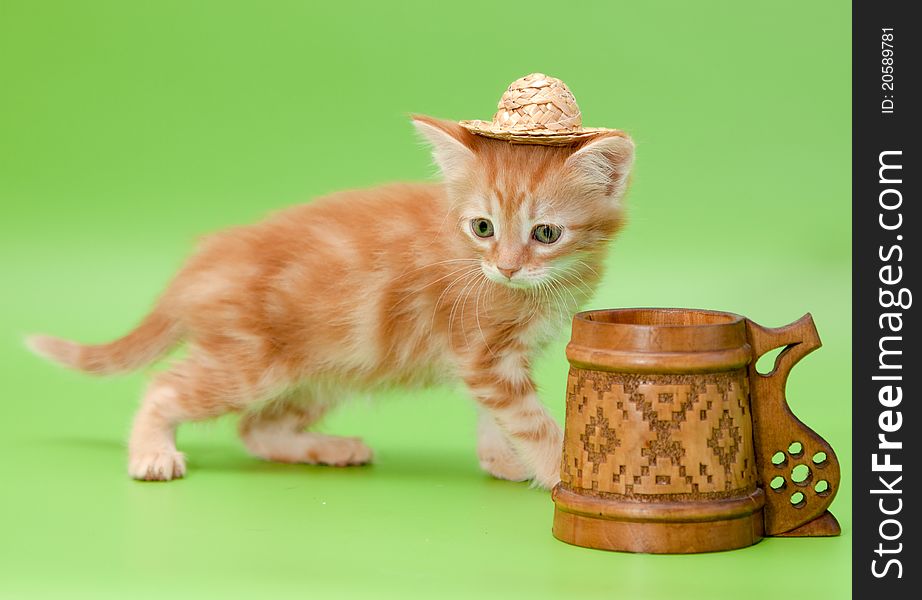 Funny and curious ginger kitten in straw and carved mug isolated on green