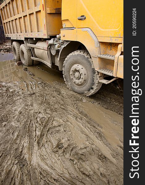 Picture of a big yellow tip lorry moving slowly on a muddy road after rain. Picture of a big yellow tip lorry moving slowly on a muddy road after rain