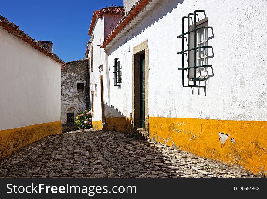 Narrow cobbled street in old medieval Obidos village, Portugal. Houses with white walls and yellow strips. Narrow cobbled street in old medieval Obidos village, Portugal. Houses with white walls and yellow strips.