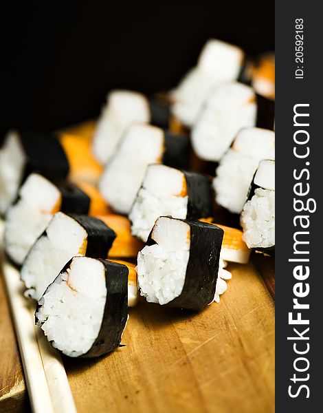 A dozen of elegantly prepared surimi and rice in a sushi type roll, on a woody beige support.