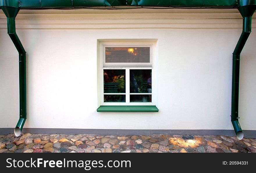 One square window on the white wall, two green downspouts. One square window on the white wall, two green downspouts.