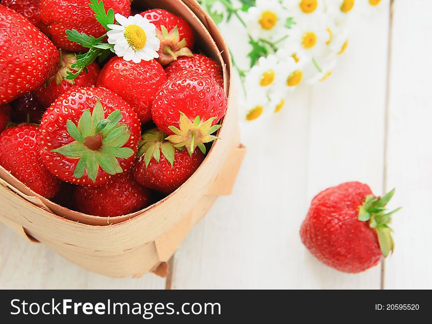 Fresh strawberry in a basket with daisies on a white table