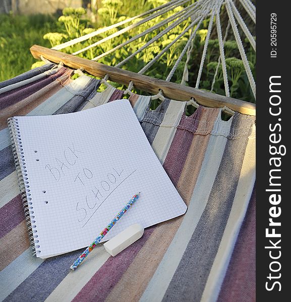 Paper and pencil with written phrase back to school in a hammock symbolizing end of summer holiday or start of semester.