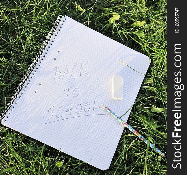 Paper, pencil and erasure laying on the grass in the afternoon sun symbolizing end of summer holiday or start of a new term.