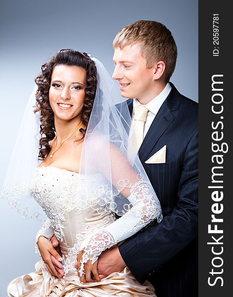 Studio portrait of young elegant enamoured just married groom looking at beautiful bride and embracing on blue background. Studio portrait of young elegant enamoured just married groom looking at beautiful bride and embracing on blue background