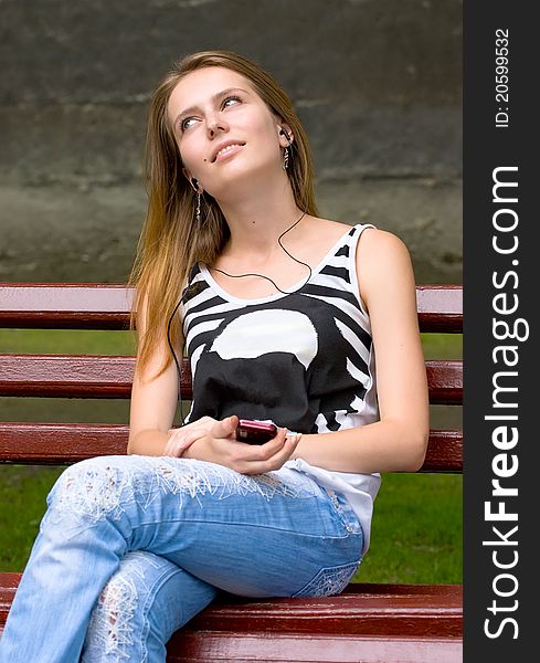 Cute attractive girl is listening music in earphones plugs on mp3 player or mobile phone. Cute attractive girl is listening music in earphones plugs on mp3 player or mobile phone