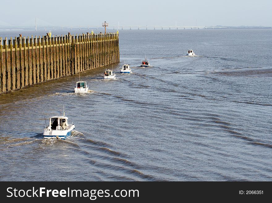 Six fishing boats head out past a pier for a day at sea. Six fishing boats head out past a pier for a day at sea