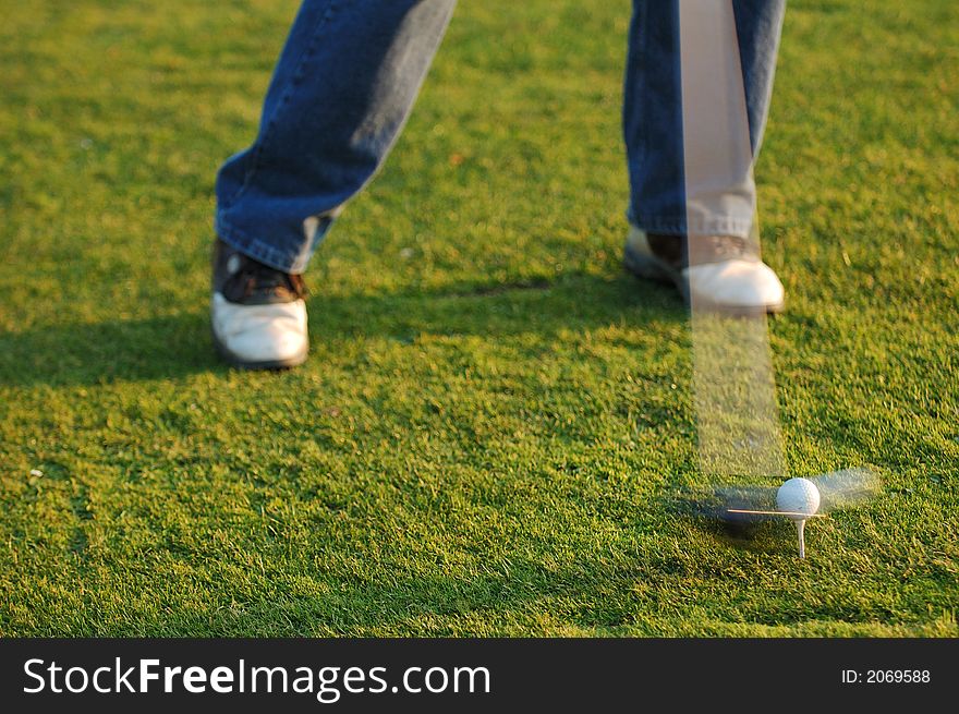 Golfer in swing as head of club hits ball in motion demonstrating the speed of the head of the club. Golfer in swing as head of club hits ball in motion demonstrating the speed of the head of the club