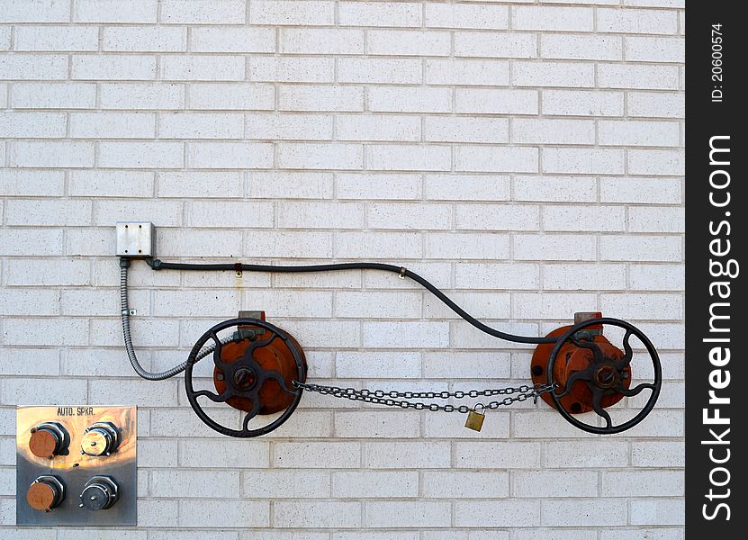 A unique vehicle-like design created from conduits, two round fire hose water shut off valves and a safety chain against the side of a white brick building. A unique vehicle-like design created from conduits, two round fire hose water shut off valves and a safety chain against the side of a white brick building.