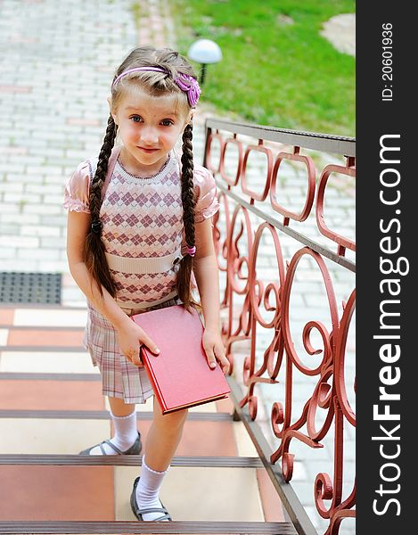 Young school girl with pink backpack stands on stairs with a book in hands. Young school girl with pink backpack stands on stairs with a book in hands