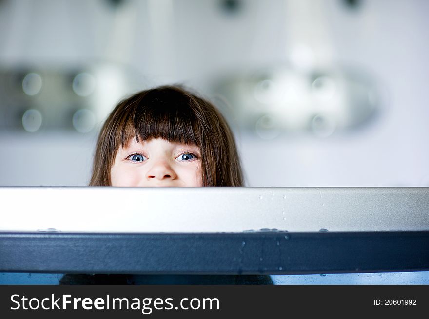 Child girl plays in a bathtub while looking out over a side