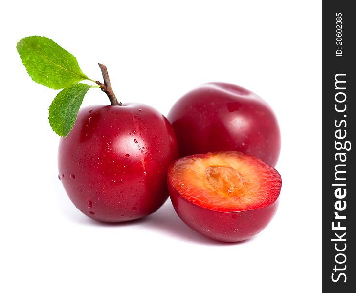 Two fresh plums and a half with leafs isolated on white background