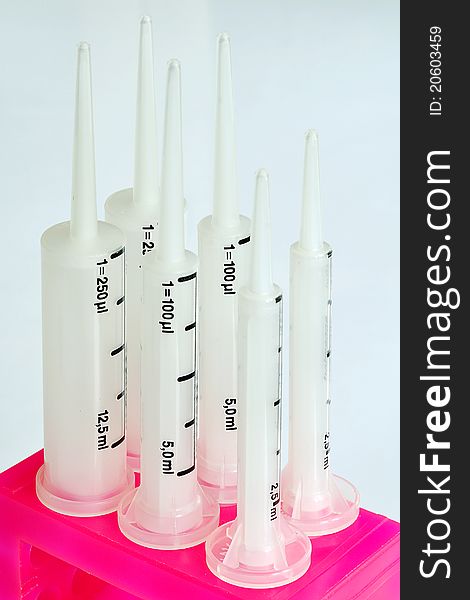 A row of white syringe pipets with pink stand. A row of white syringe pipets with pink stand