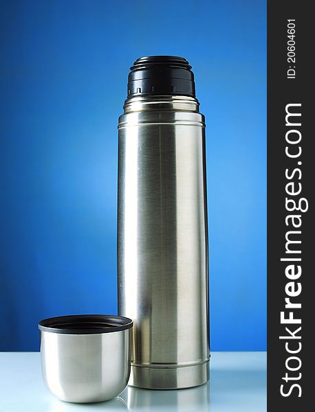 Thermos mug on the table and, on a blue background. Thermos mug on the table and, on a blue background