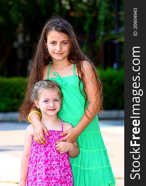 Two little girls,(sisters) holding each-other outdoor looking at the camera. Two little girls,(sisters) holding each-other outdoor looking at the camera