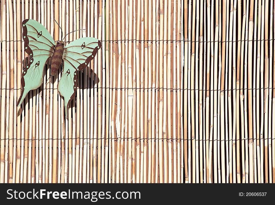 An artistic metal butterfly sits on a bamboo fence in an urban yard.