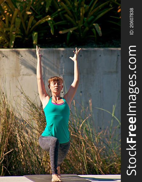An athletic brown haired woman is doing yoga exercise Virabhadrasana or warrior 1 pose outside in park in direct sunlight. An athletic brown haired woman is doing yoga exercise Virabhadrasana or warrior 1 pose outside in park in direct sunlight.
