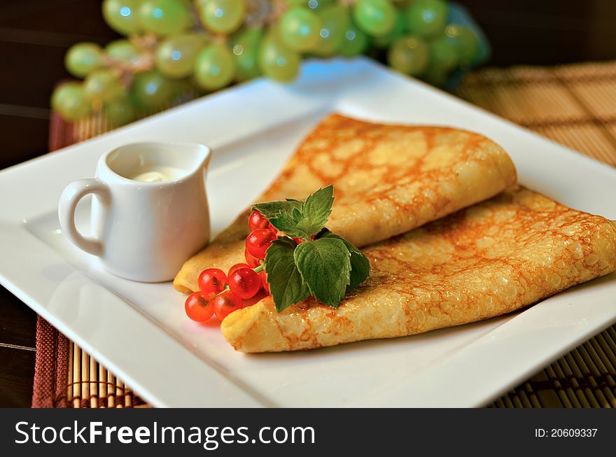 Russian pancakes with sour cream, redcurrant and mint