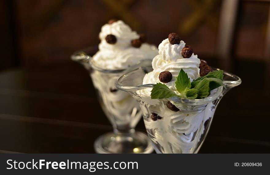 Whipped cream dessert with chocolate balls and mint on brown background