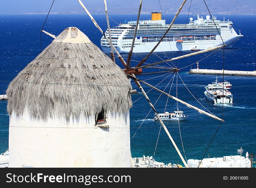 Traditional mykonian windmill and a very big cruise liner at anchor in the blue sea. Traditional mykonian windmill and a very big cruise liner at anchor in the blue sea