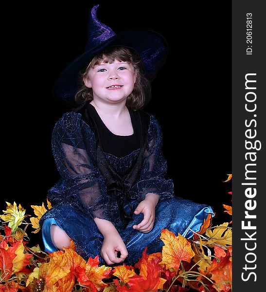 Adorable little girl in witch costume with leaves