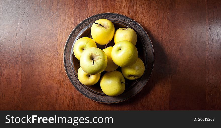 A plate of golden delicious apples on a wooden table viewed from above. A plate of golden delicious apples on a wooden table viewed from above