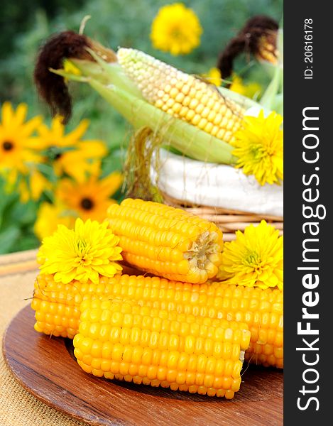 Cooked and raw corncobs with yellow flowers on the background. Cooked and raw corncobs with yellow flowers on the background.