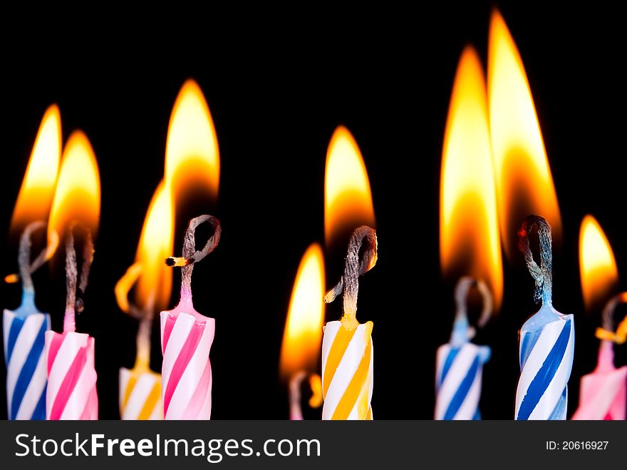 Many coloured candles burn before black background